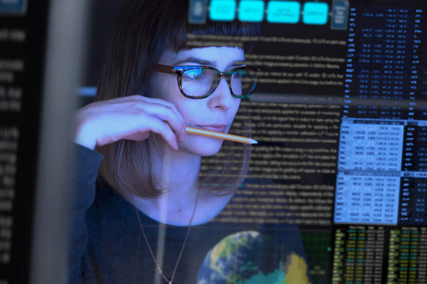 woman with glasses looks at several computer screens
